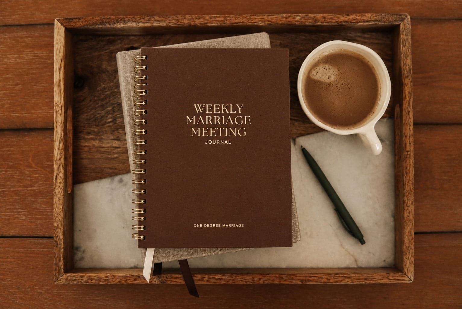 The spiral-bound Weekly Marriage Meeting Journal on a wooden tray with coffee