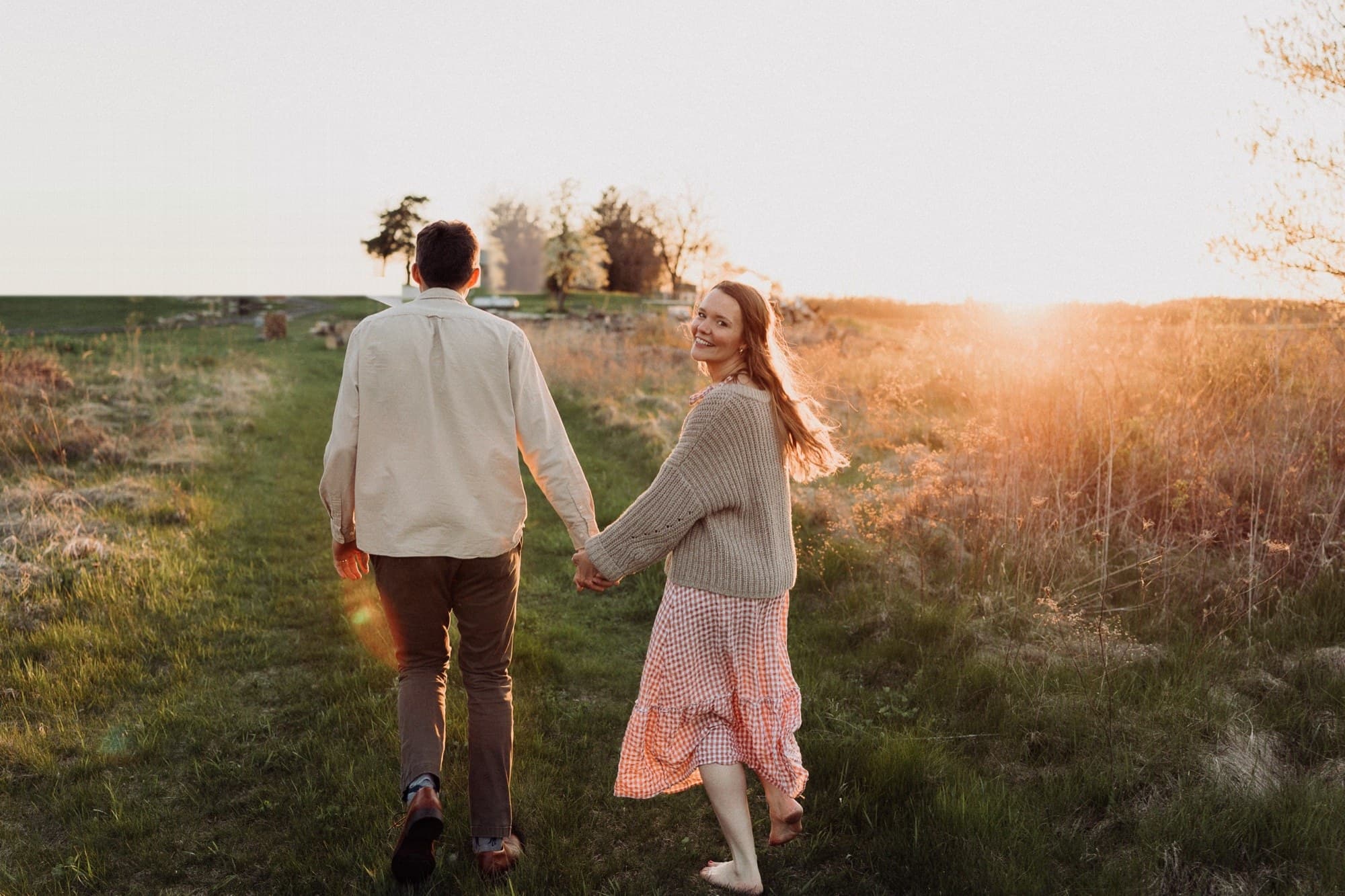 Xan and Nathaniel walking hand in hand through a field at sunset